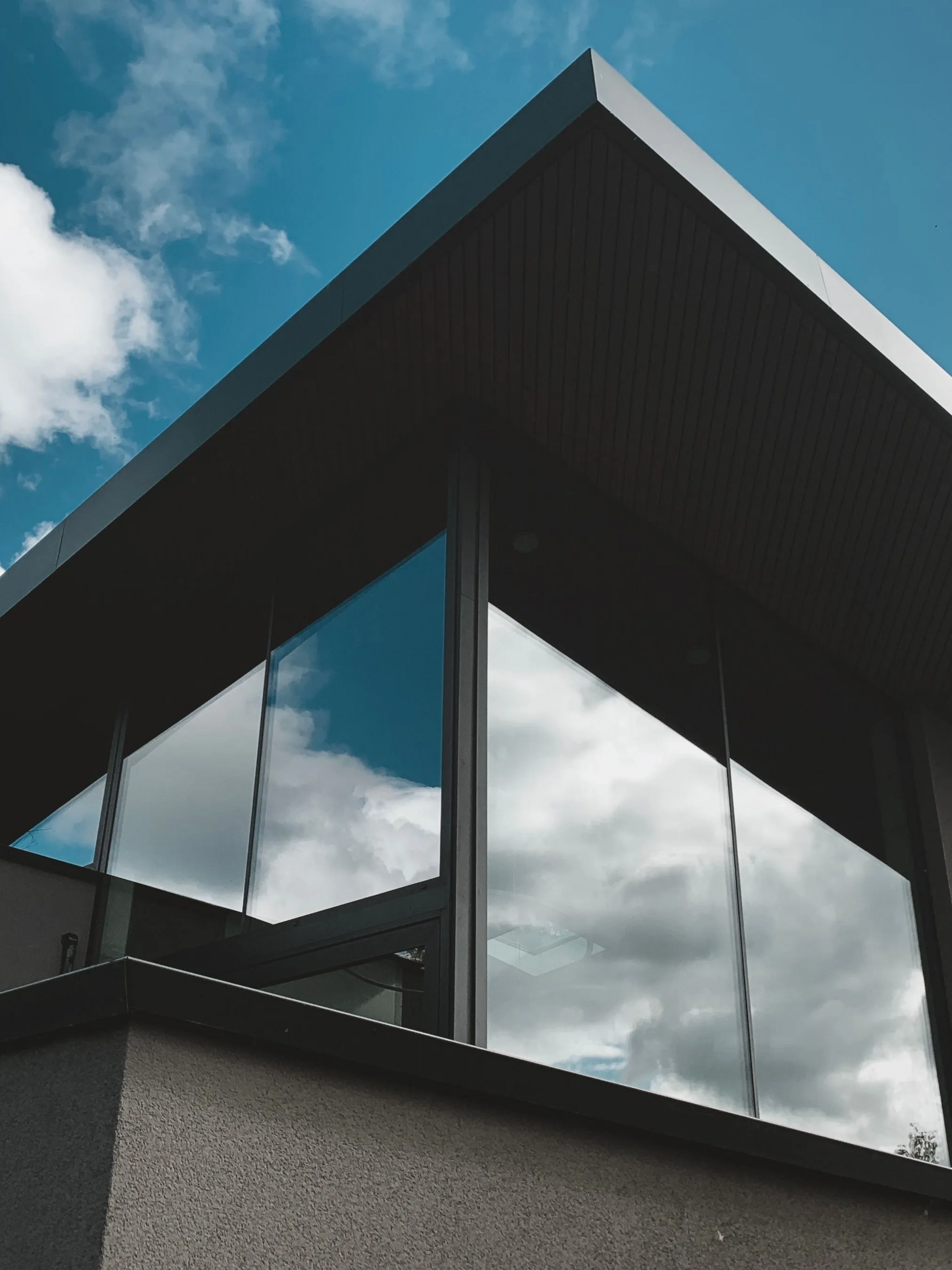 Modern building corner with dark roof and reflective glass windows under a blue sky