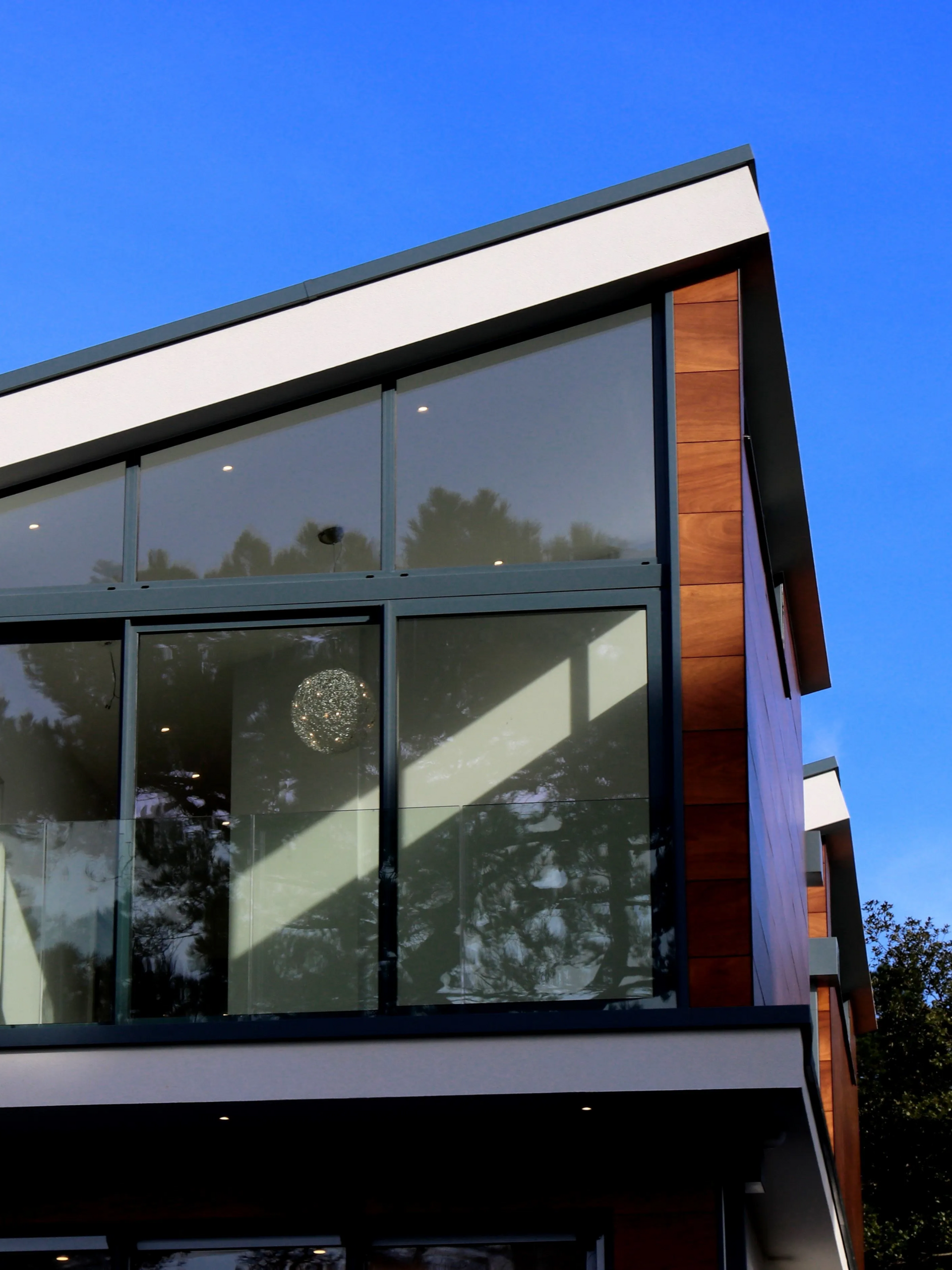 Modern two-story building facade with large glass windows and wood siding against a blue sky