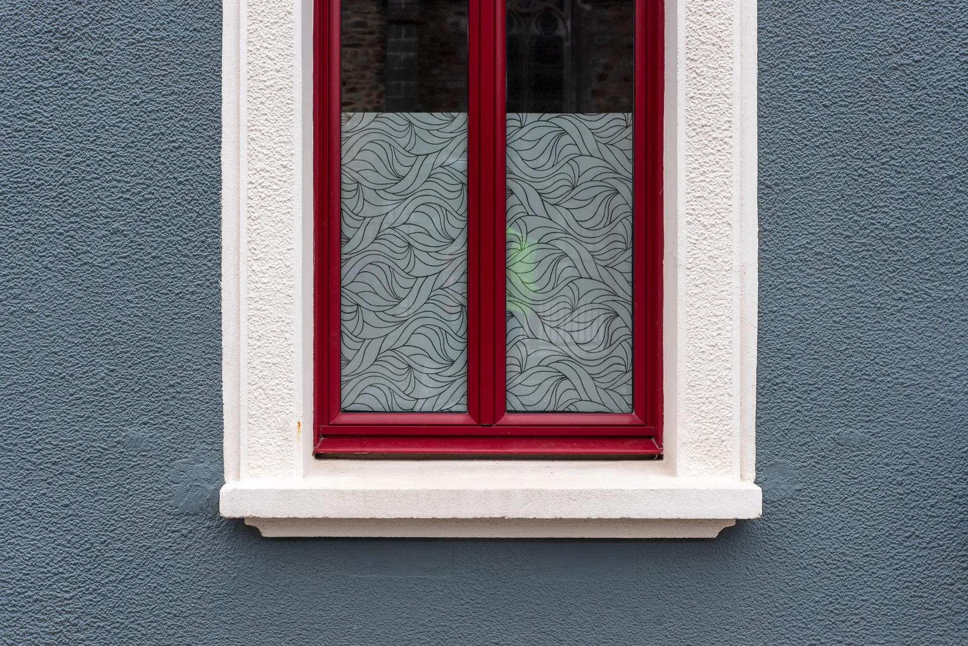 Red-framed window with frosted glass set in a white-trimmed blue wall
