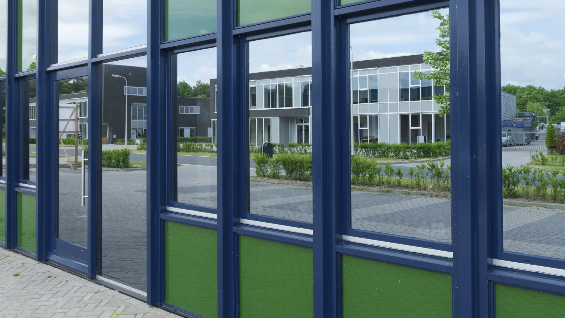 Glass storefront windows reflecting a modern building across a paved courtyard