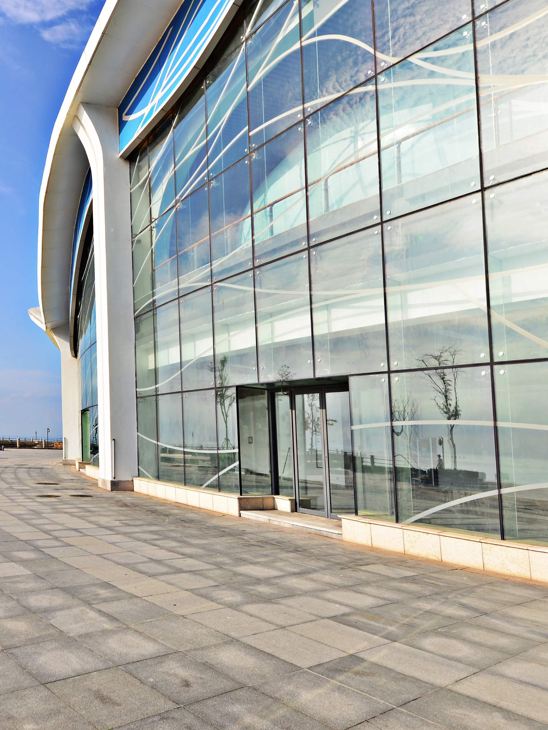 Modern glass-front building exterior with curved façade and paved walkway