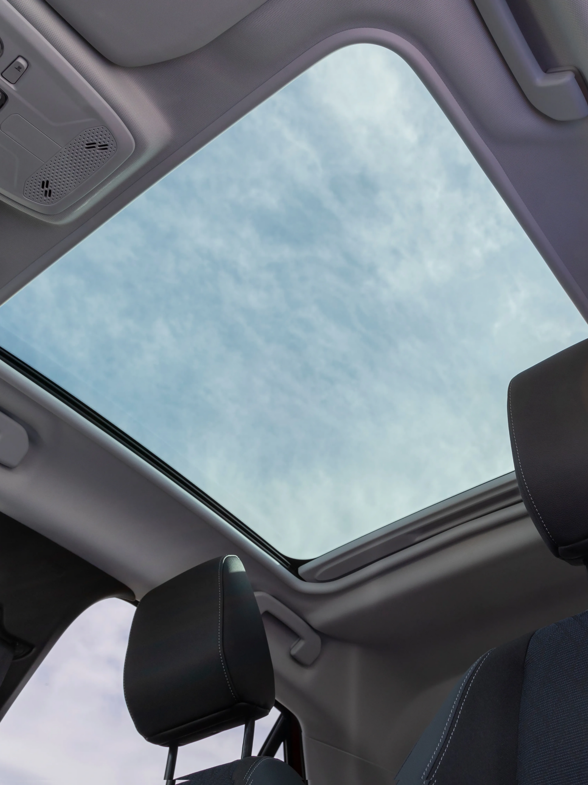Car interior with a panoramic sunroof showing a cloudy sky