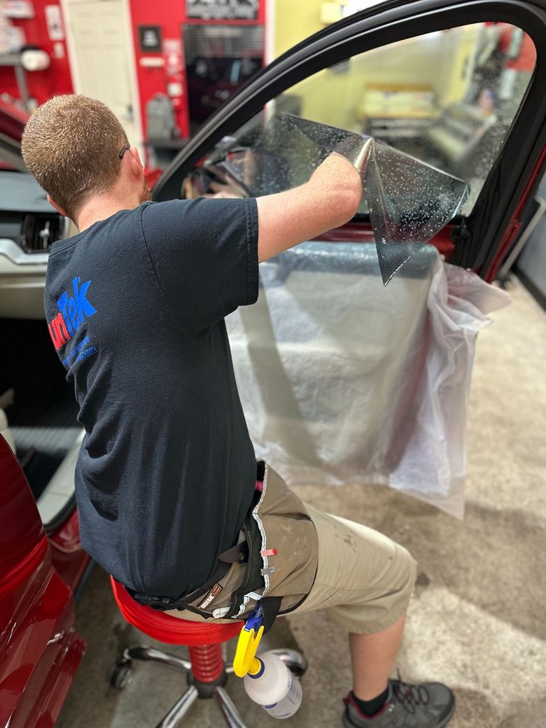 Technician applying window tint film to a car door window in a garage