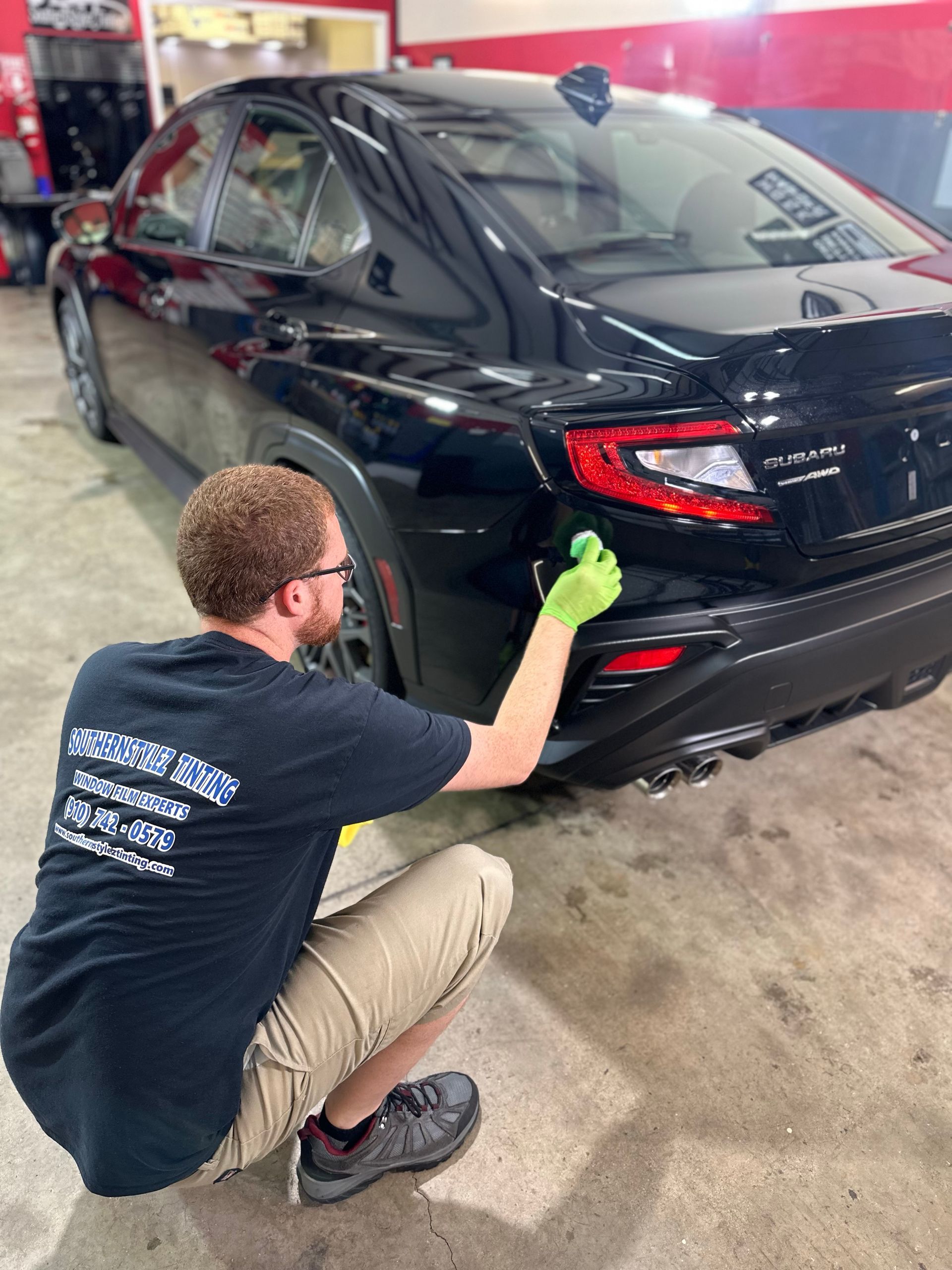 Detailing technician polishing the rear of a black sedan in a garage.