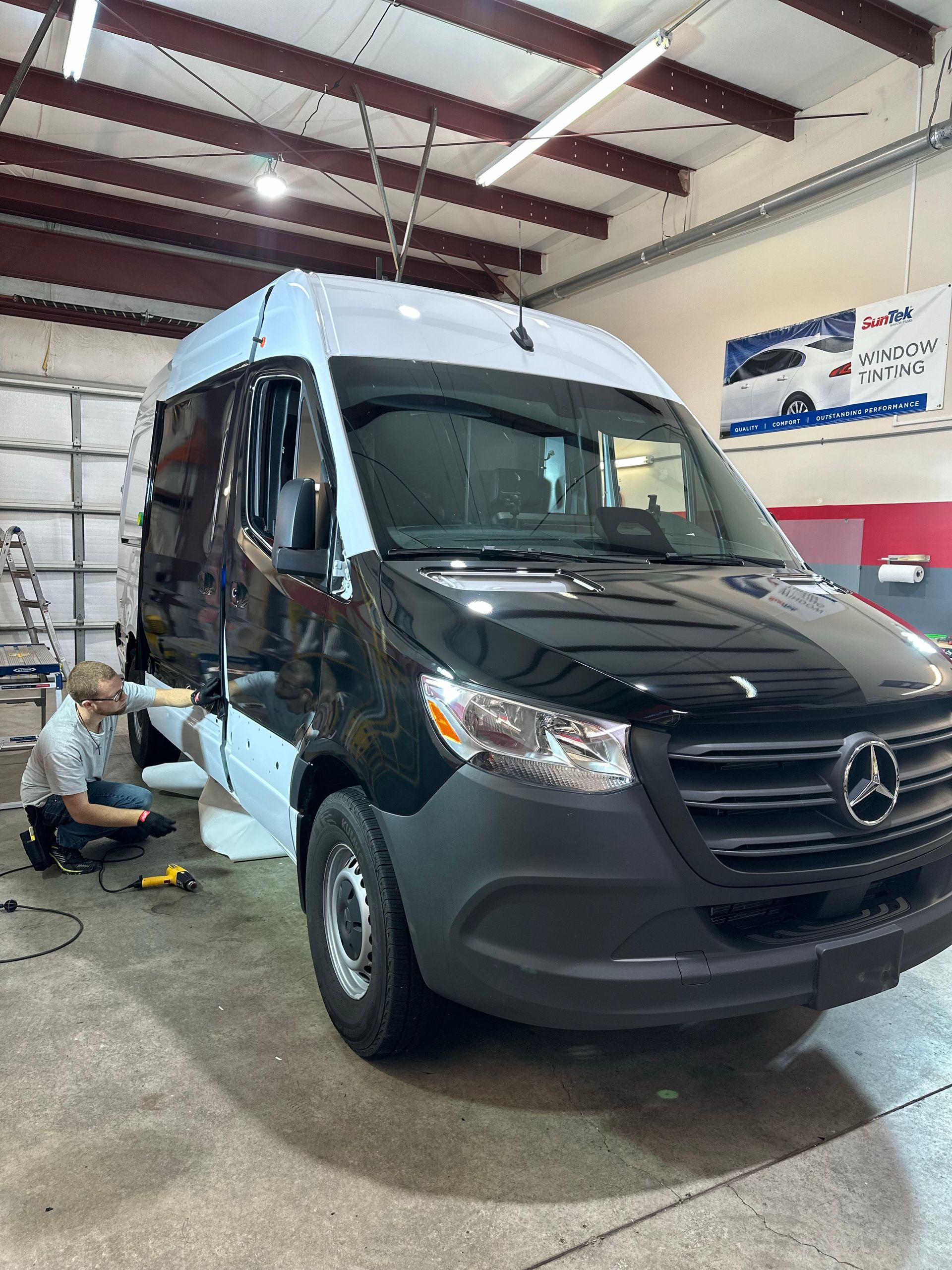 Black Mercedes van in a garage with a mechanic working near the front wheel
