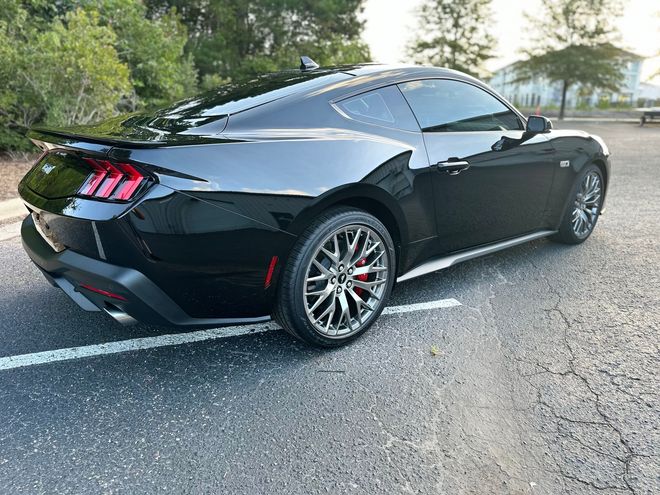 Black sports coupe parked on a street, rear three-quarter view with red taillights and a spoiler