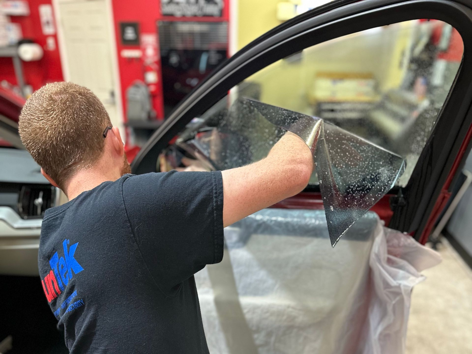 Gloved hands applying red vinyl wrap to a car hood with a heat gun