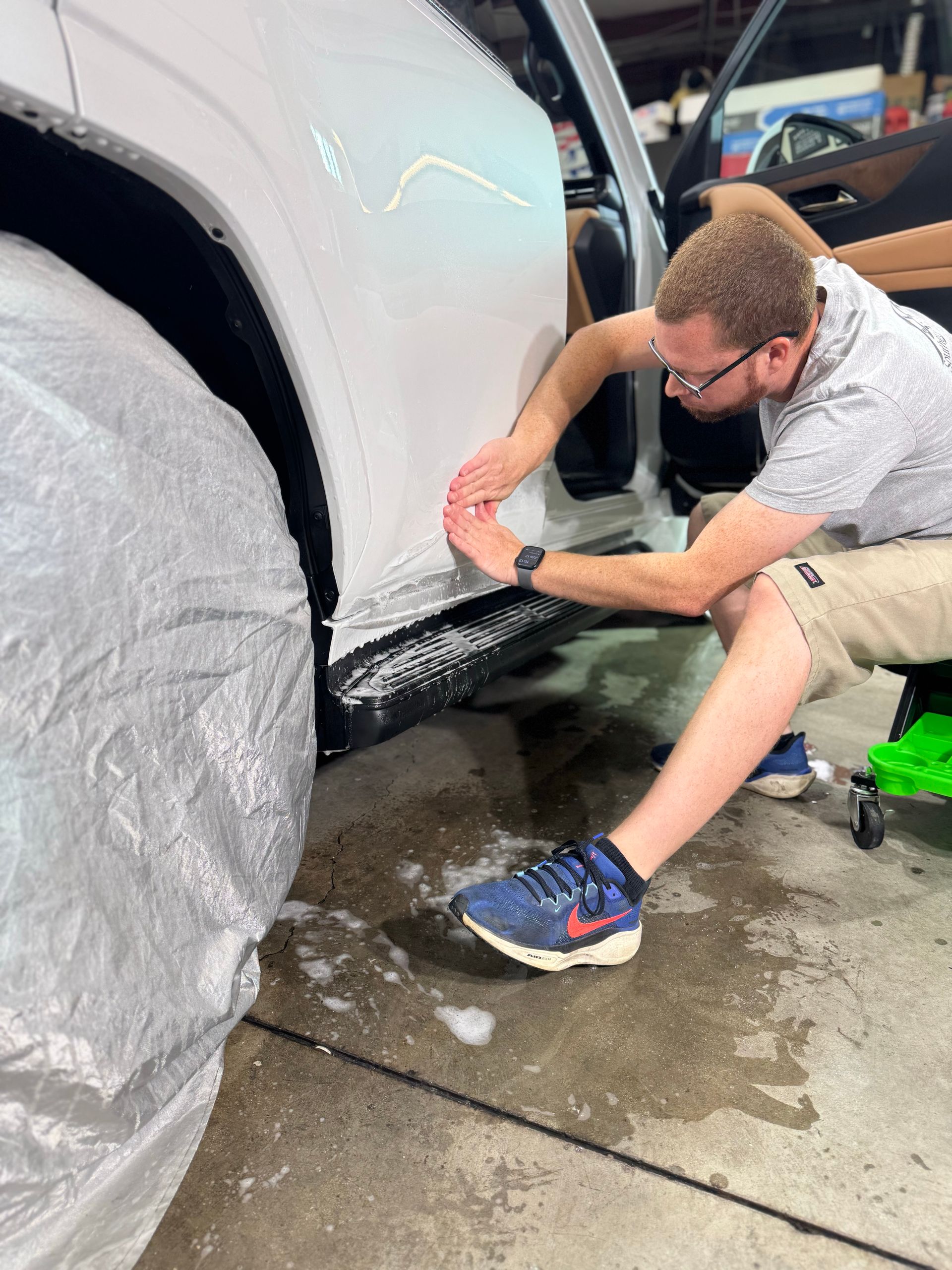 Gloved hands applying red vinyl wrap to a car hood with a heat gun