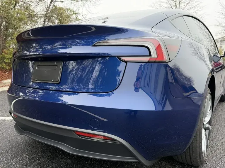 Blue Tesla sedan rear view parked outdoors on a tree-lined street
