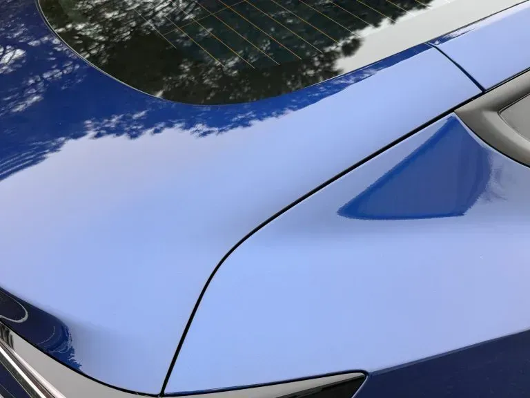 Close-up of a shiny blue car hood and windshield reflecting trees and sky