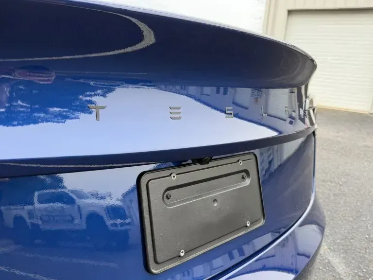Close-up of a blue car’s rear with a blank license plate holder and trunk lid