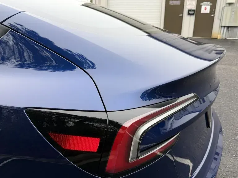 Rear corner of a blue car with a red-and-white taillight in a driveway or garage