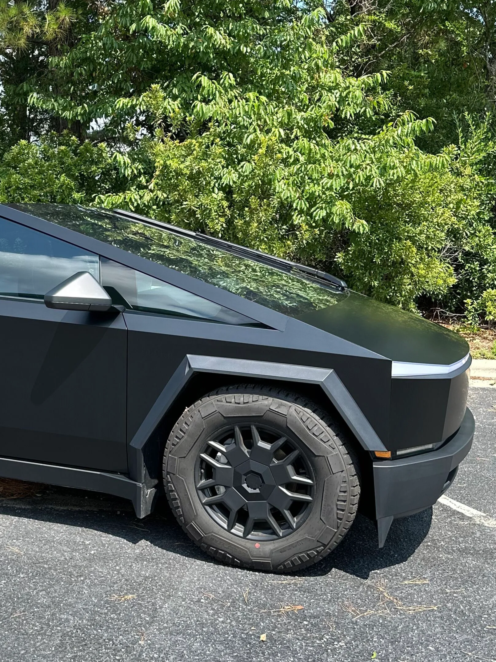 Black angular pickup truck front wheel parked on a road beside green trees