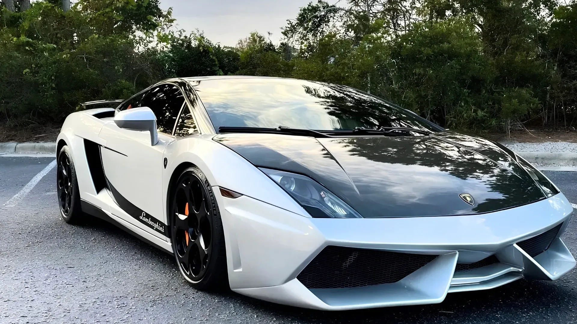 White sports car with black hood parked on a gravel road beside trees