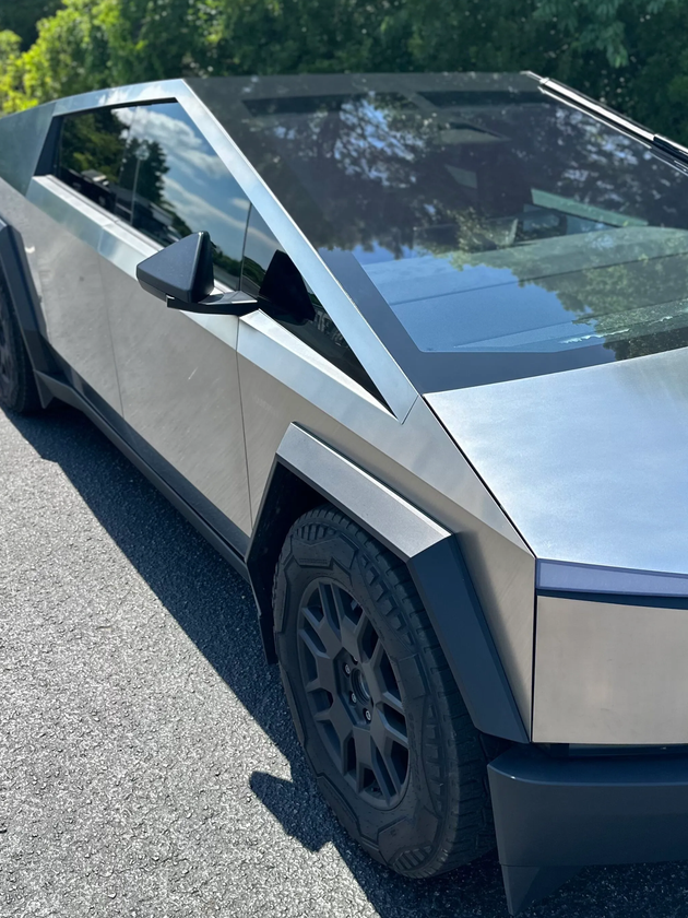 Silver Tesla Cybertruck parked on a road beside trees