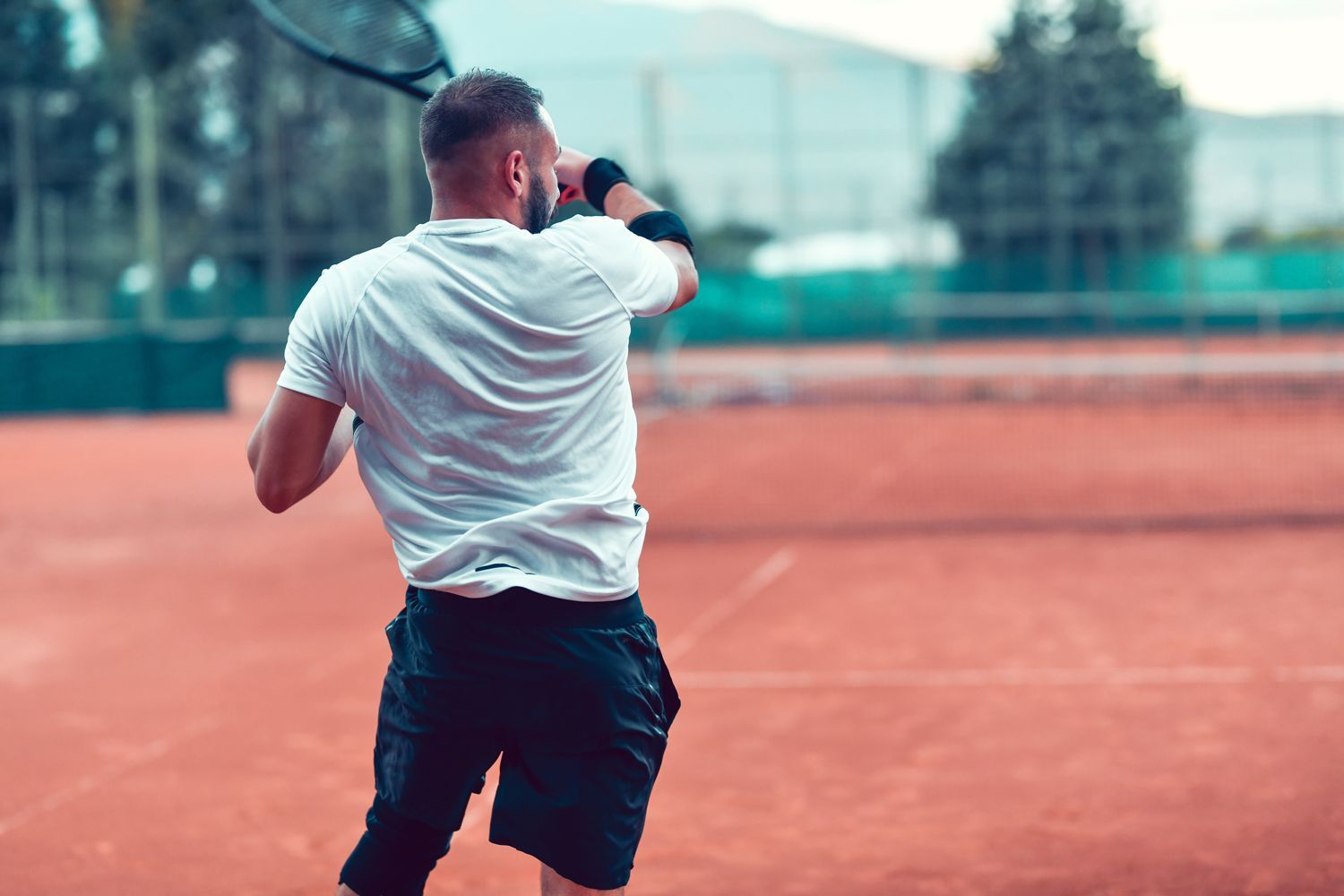 Man in white shirt and black shorts playing tennis on a clay court.