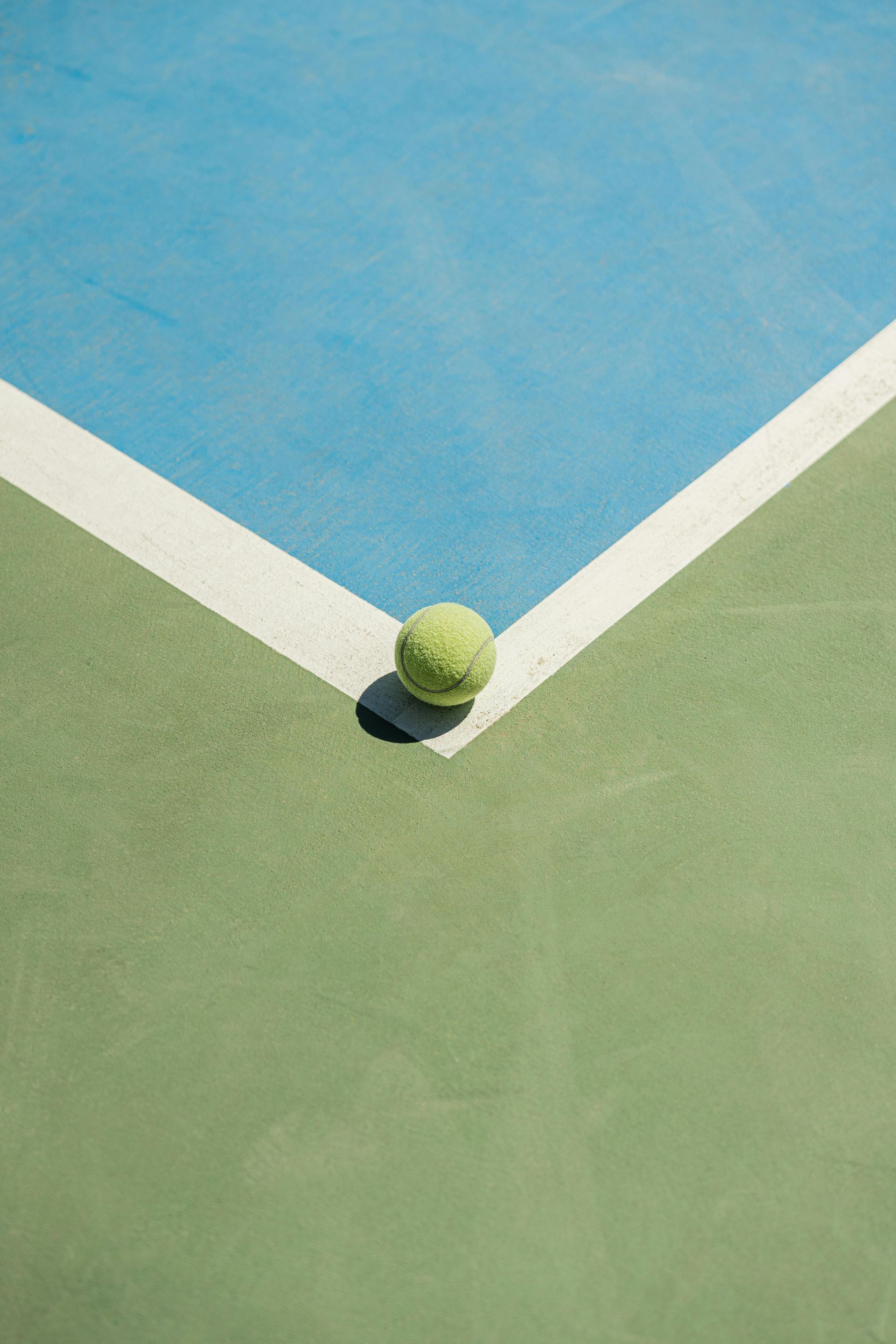 Tennis ball at the corner of a green and blue court, white line.