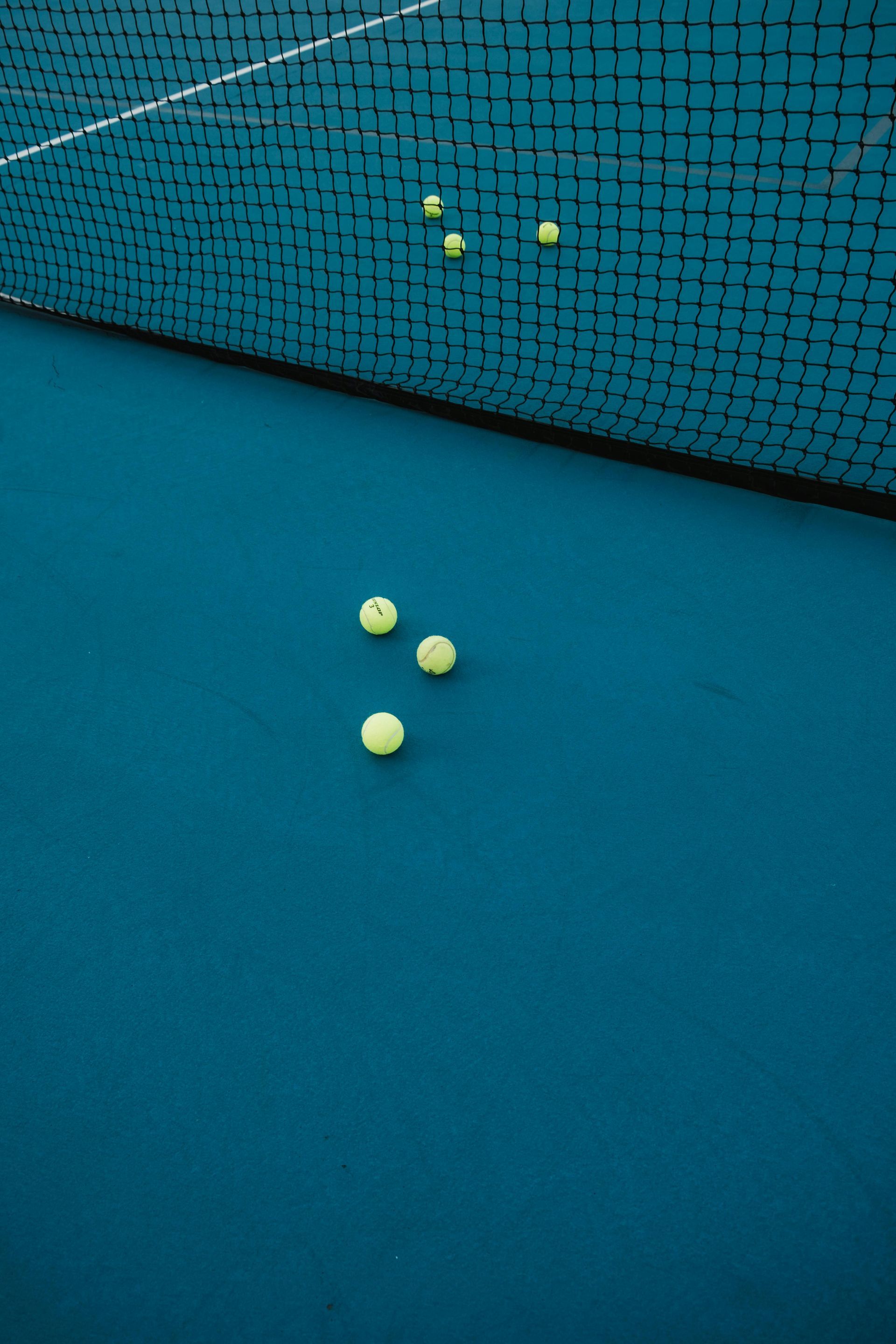 Tennis balls scattered on a blue court next to a black net.