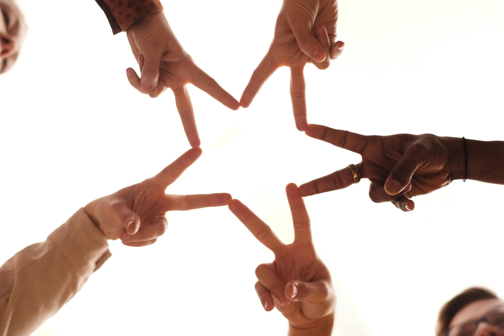 Hands of different skin tones form a star shape against a bright background.