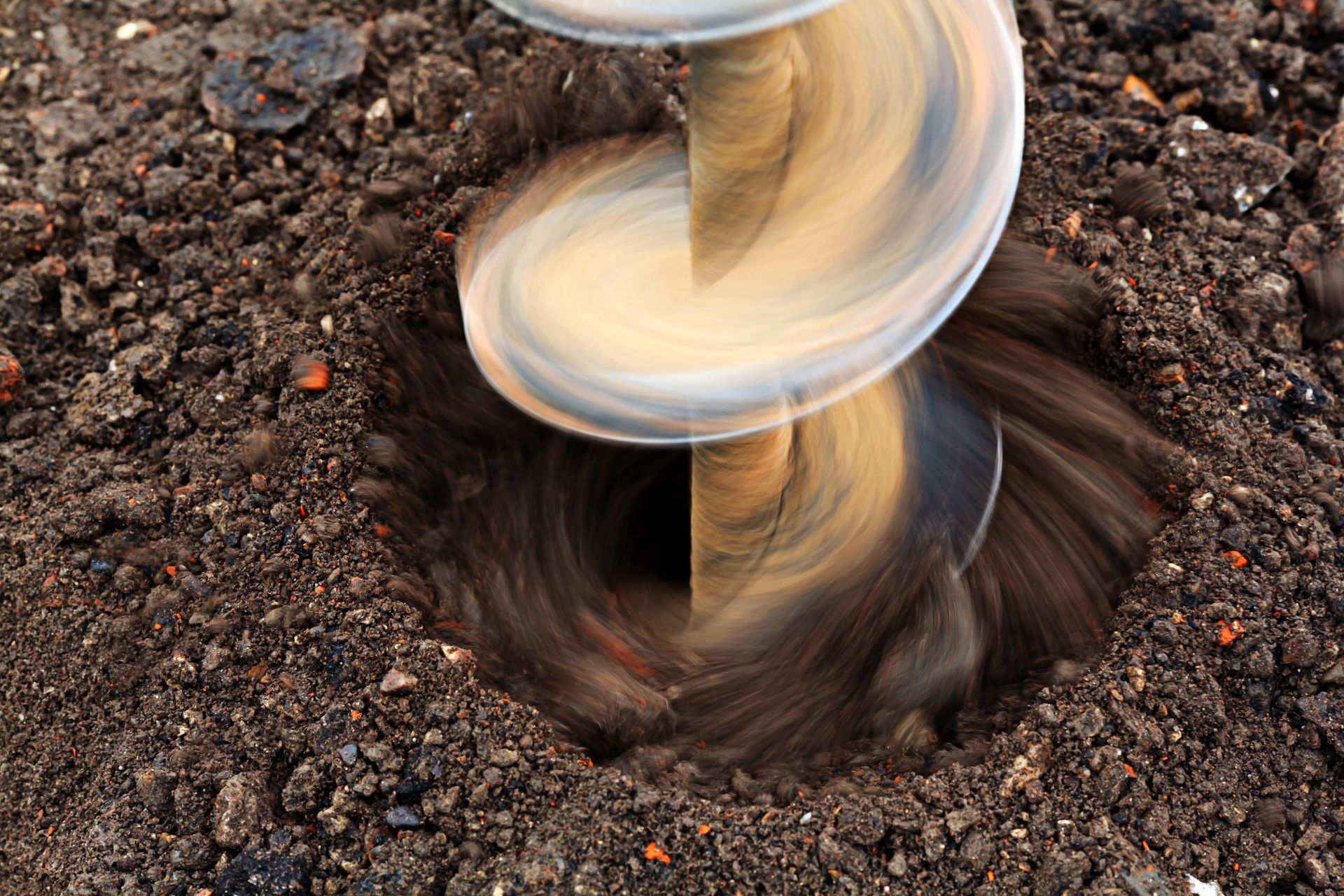 An auger drilling into dark brown soil, creating a hole.