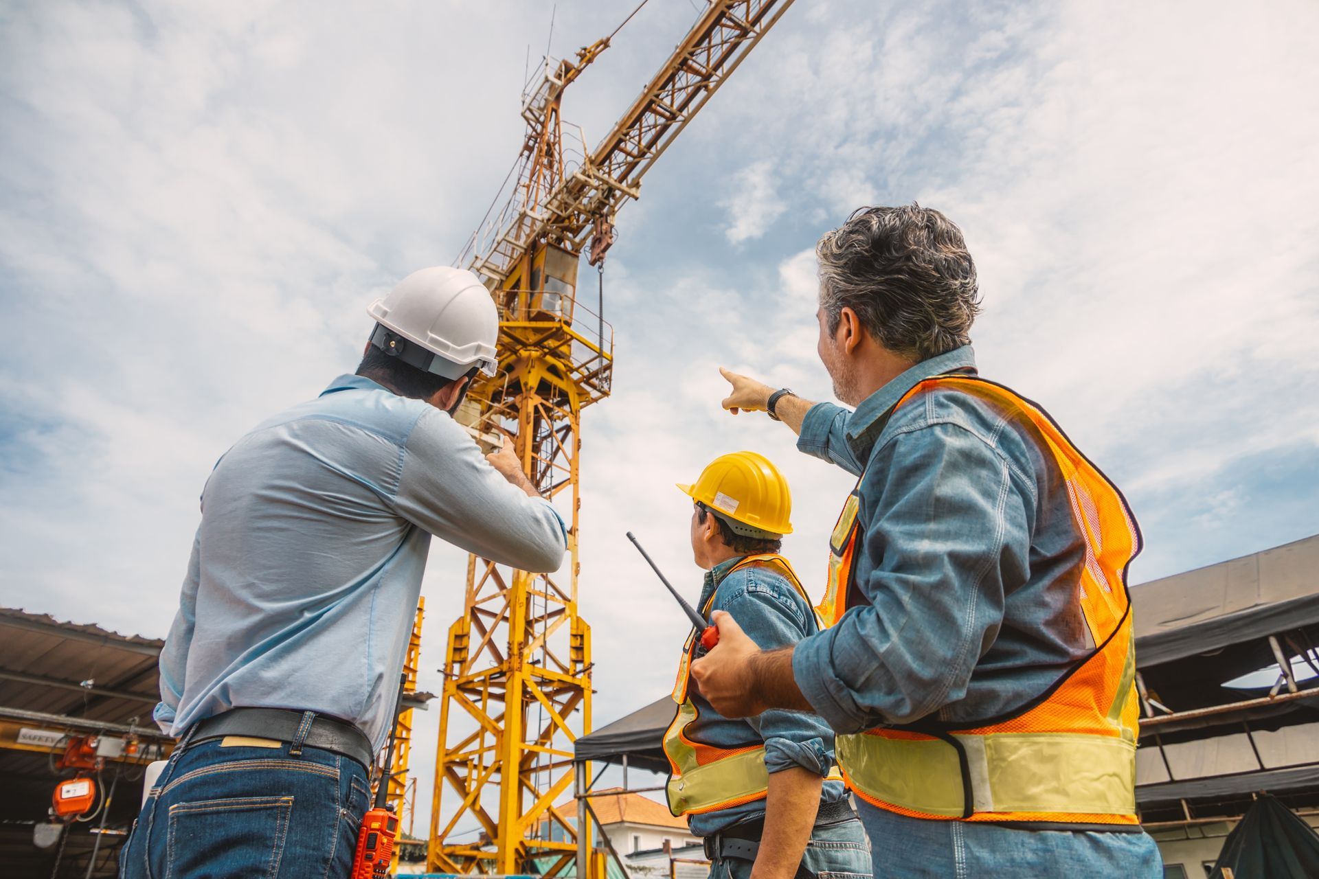 Three construction workers inspecting a crane on a sunny day. One points upward.