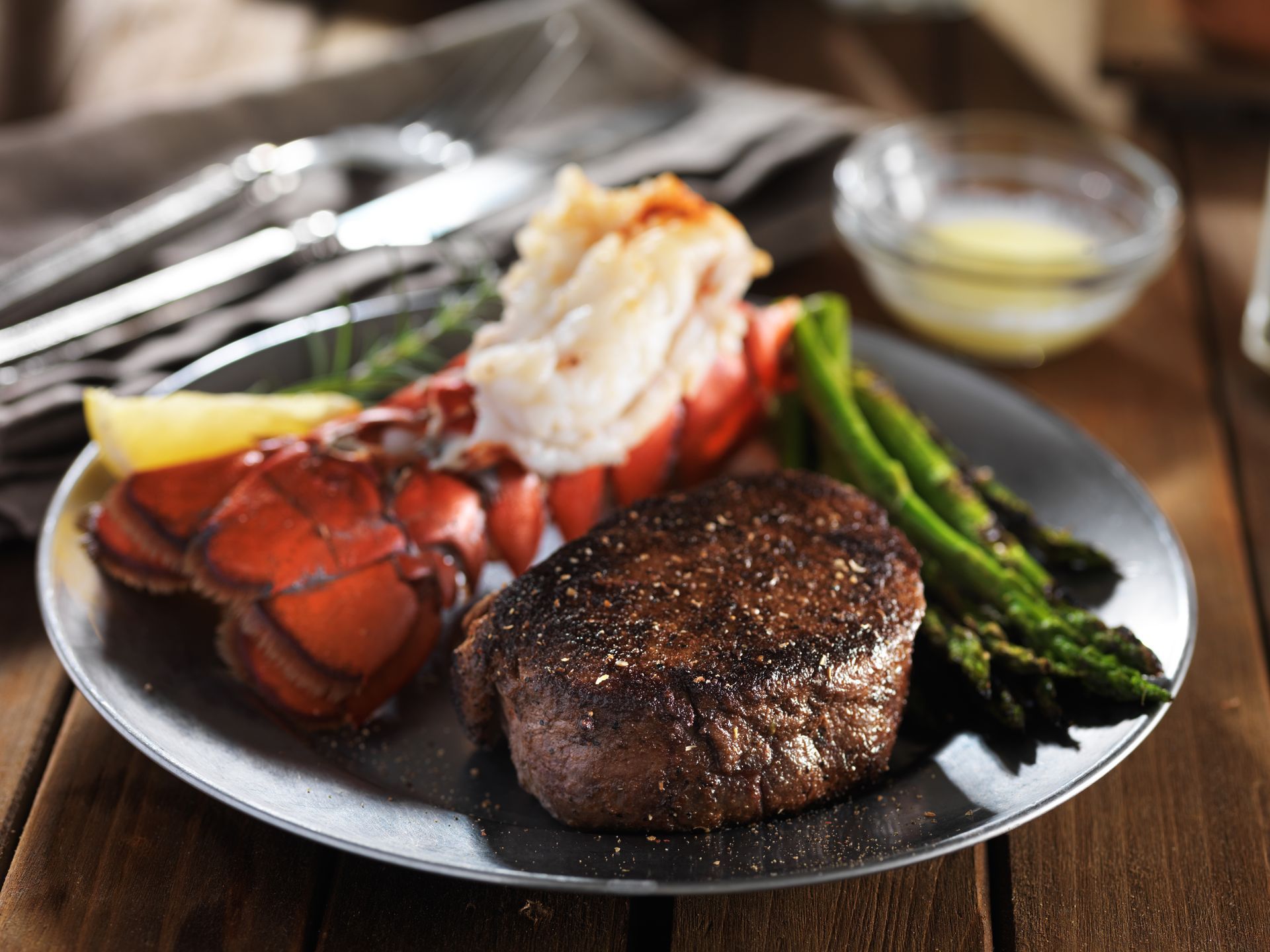 Steak and lobster tail with asparagus on a plate, served with lemon and butter sauce