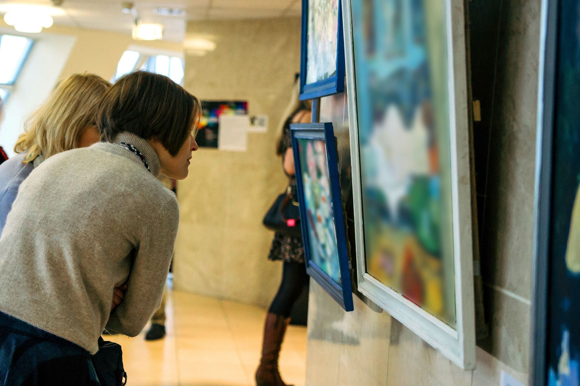 Two people lean in to view framed photos displayed along a gallery wall.