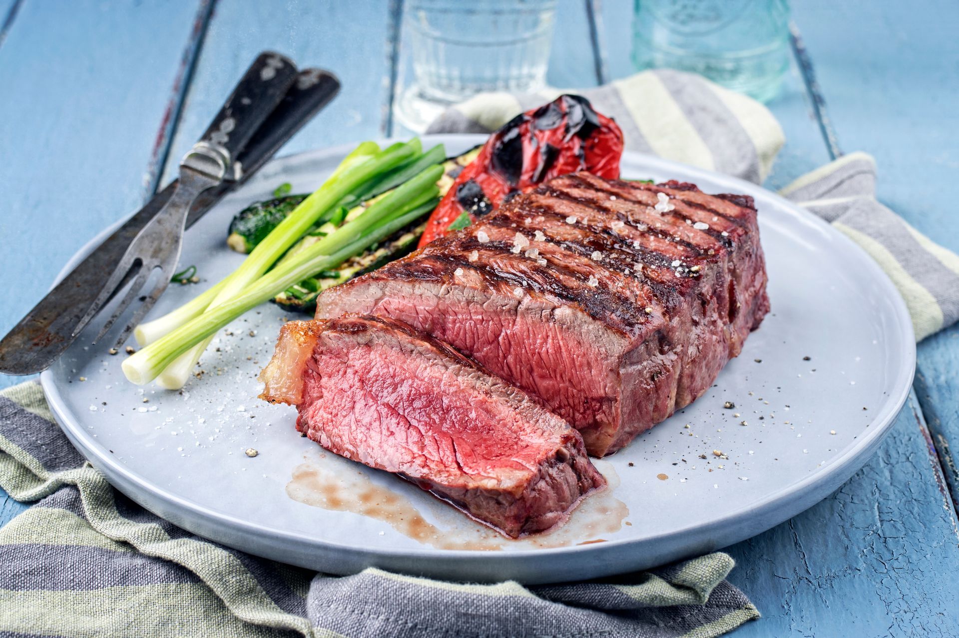 Grilled steak with asparagus and cherry tomatoes on a white plate, served on a blue tablecloth
