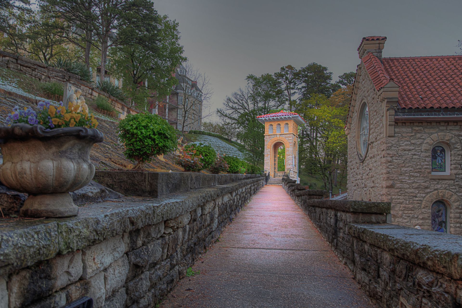 Stone walkway between old buildings leading to an illuminated archway at dusk