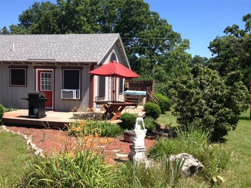Backyard patio with red umbrella, brick steps, grill, and a small house surrounded by greenery and lawn