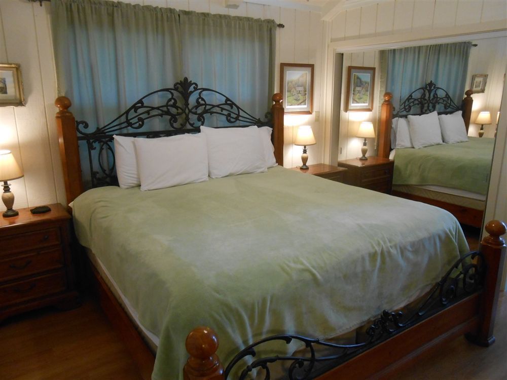 Bedroom with a wrought-iron bed, green bedding, nightstands, lamps, and a large mirror on the wall.
