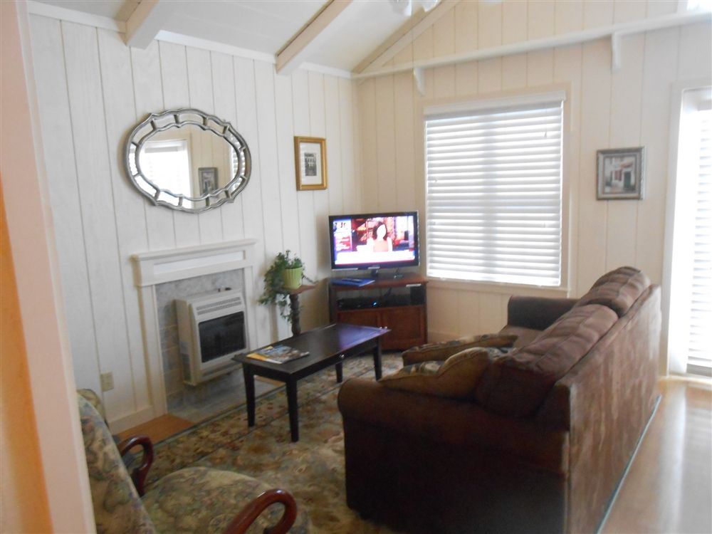 Cozy living room with a brown sofa, TV, fireplace, and large window with blinds