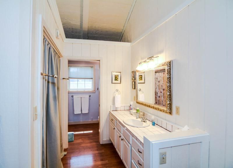 Bright white bathroom with vanity, mirror, wall sconce, and a towel rack at the far end.