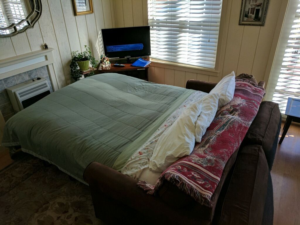 Bedroom with a bed made with green bedding and patterned pillows, near a window and TV.