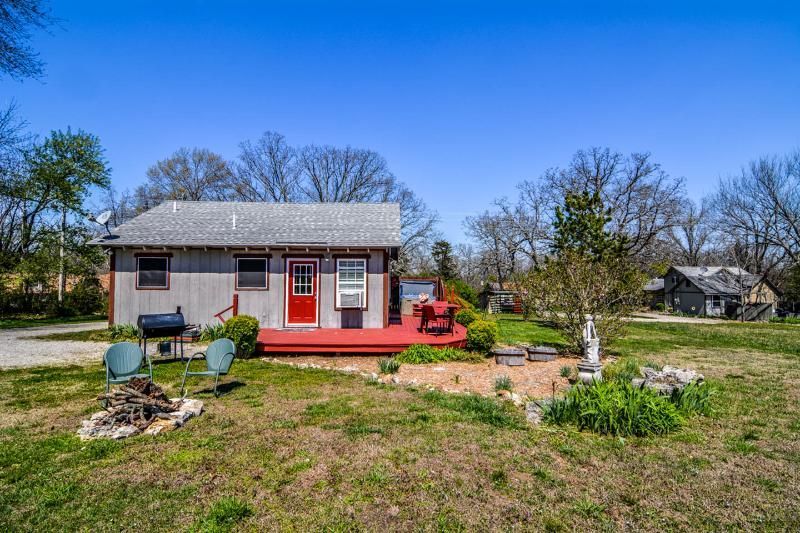 Small white house with red doors and porch in a grassy yard under a clear blue sky