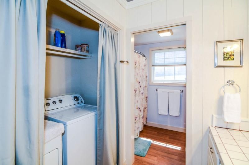 Laundry closet beside a bathroom with a washer, shelf, and blue shower curtain