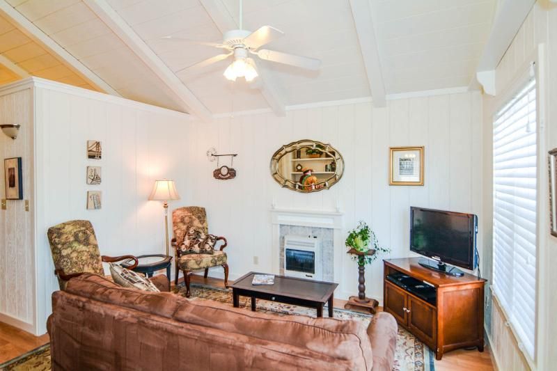 Cozy living room with brown sofa, patterned chairs, TV, and white fireplace under a vaulted ceiling