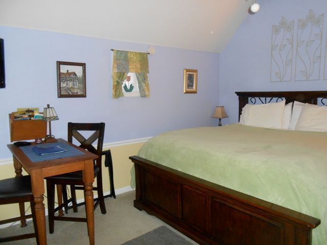 Cozy bedroom with a large bed, small desk, chair, and pale blue walls under a sloped ceiling