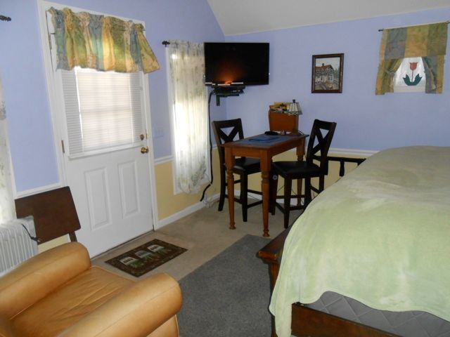 Small bedroom with a bed, desk, chair, TV, and a window with curtains.