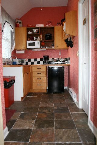 Narrow kitchen with red walls, wooden cabinets, black appliances, and dark tiled floor