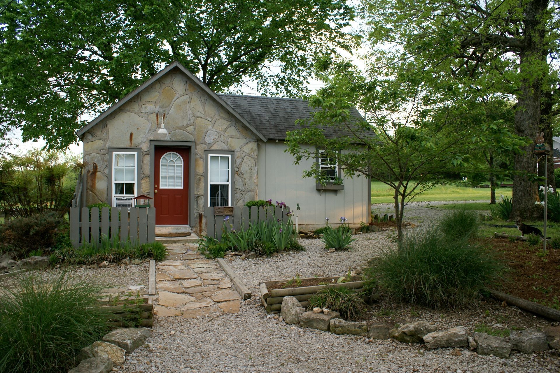 Small cottage with a red door, stone path, and garden under leafy trees