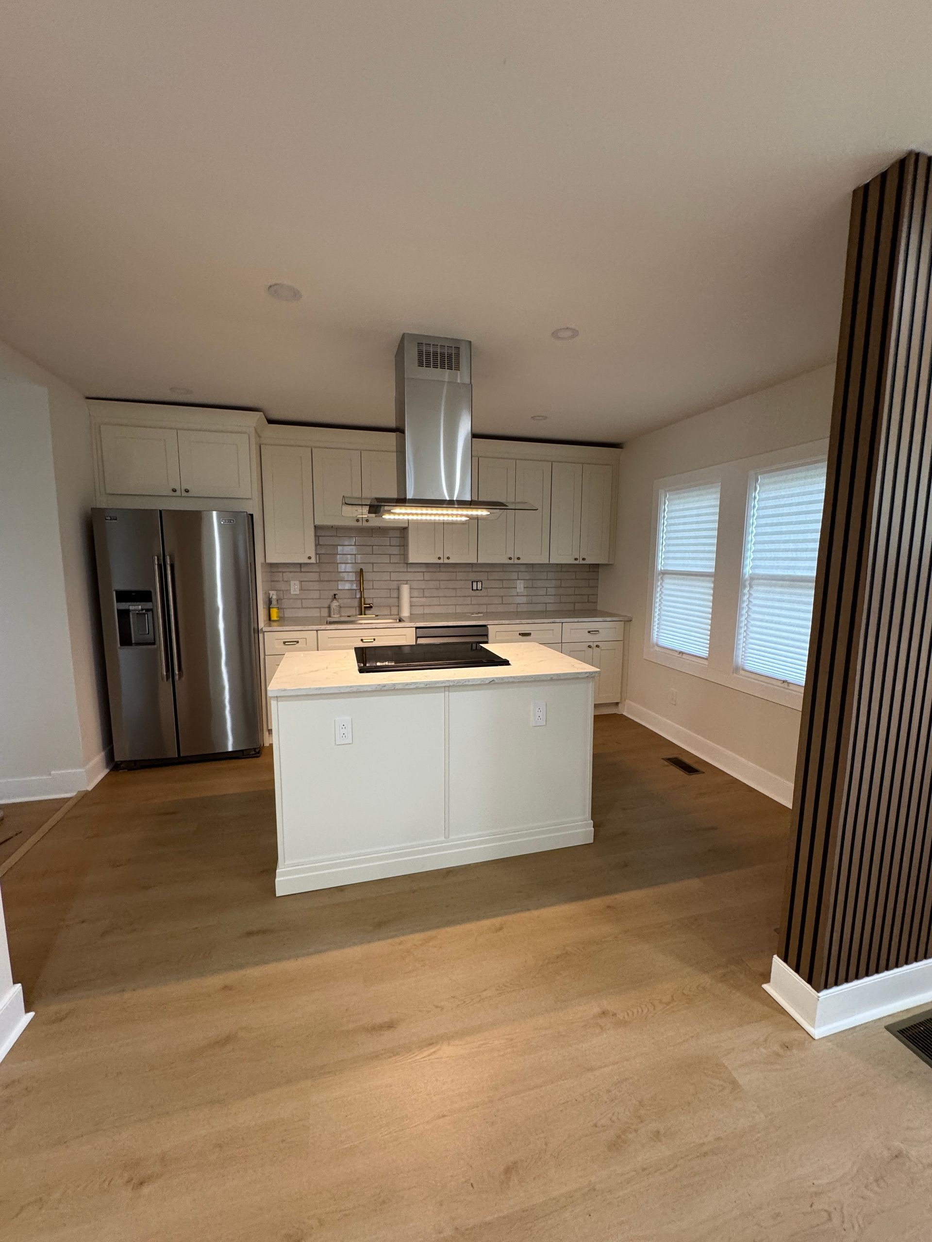 Modern kitchen with white island, stainless fridge, wood floors, and large windows