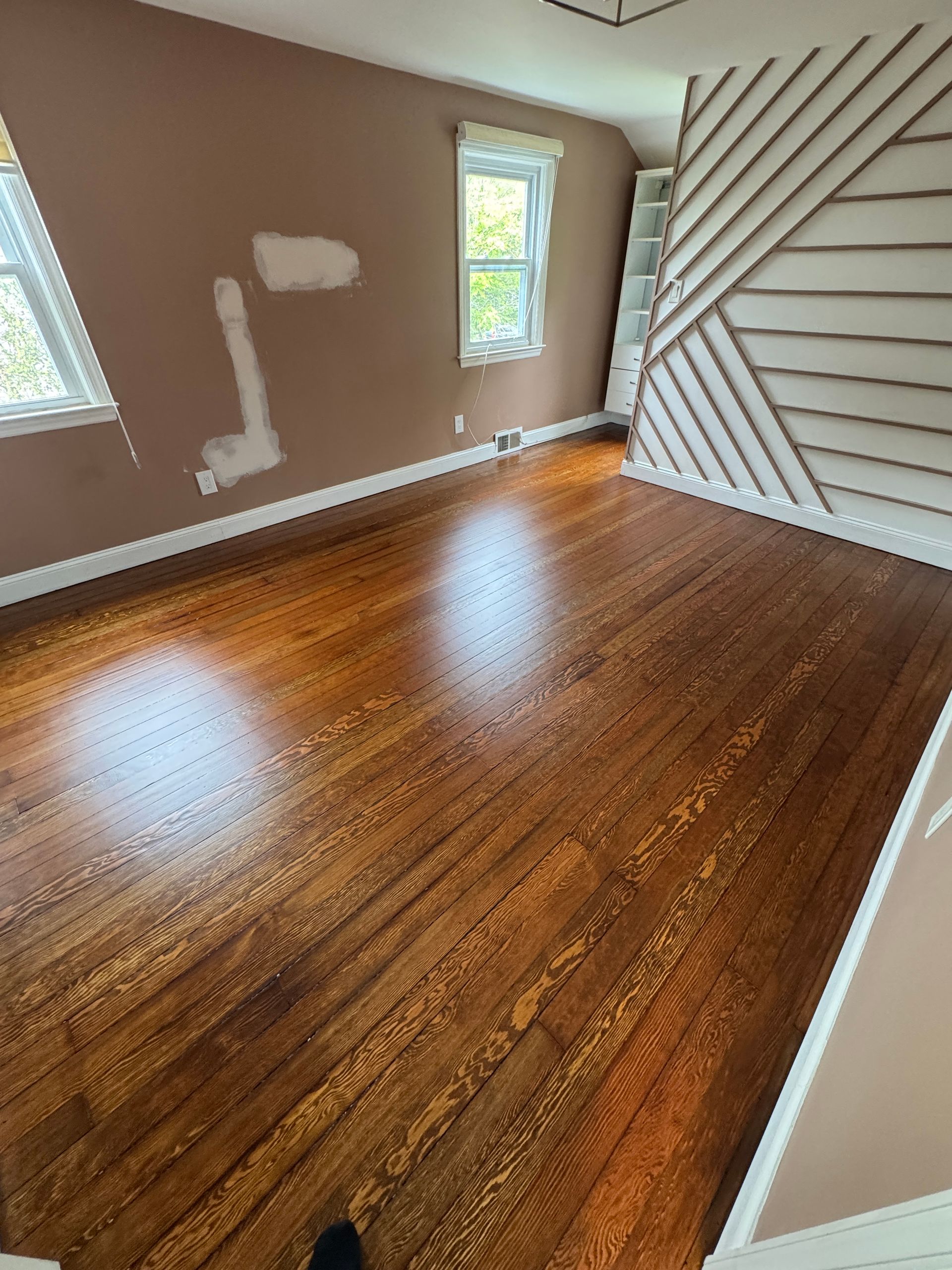 Empty room with hardwood floors, gray walls, two windows, and a staircase with diagonal slats