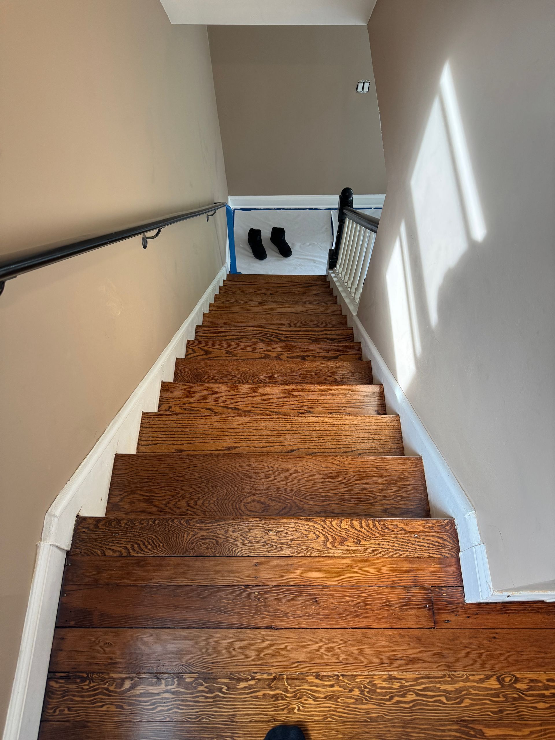 Wooden staircase with metal handrails, leading down to a bright hallway at the bottom.