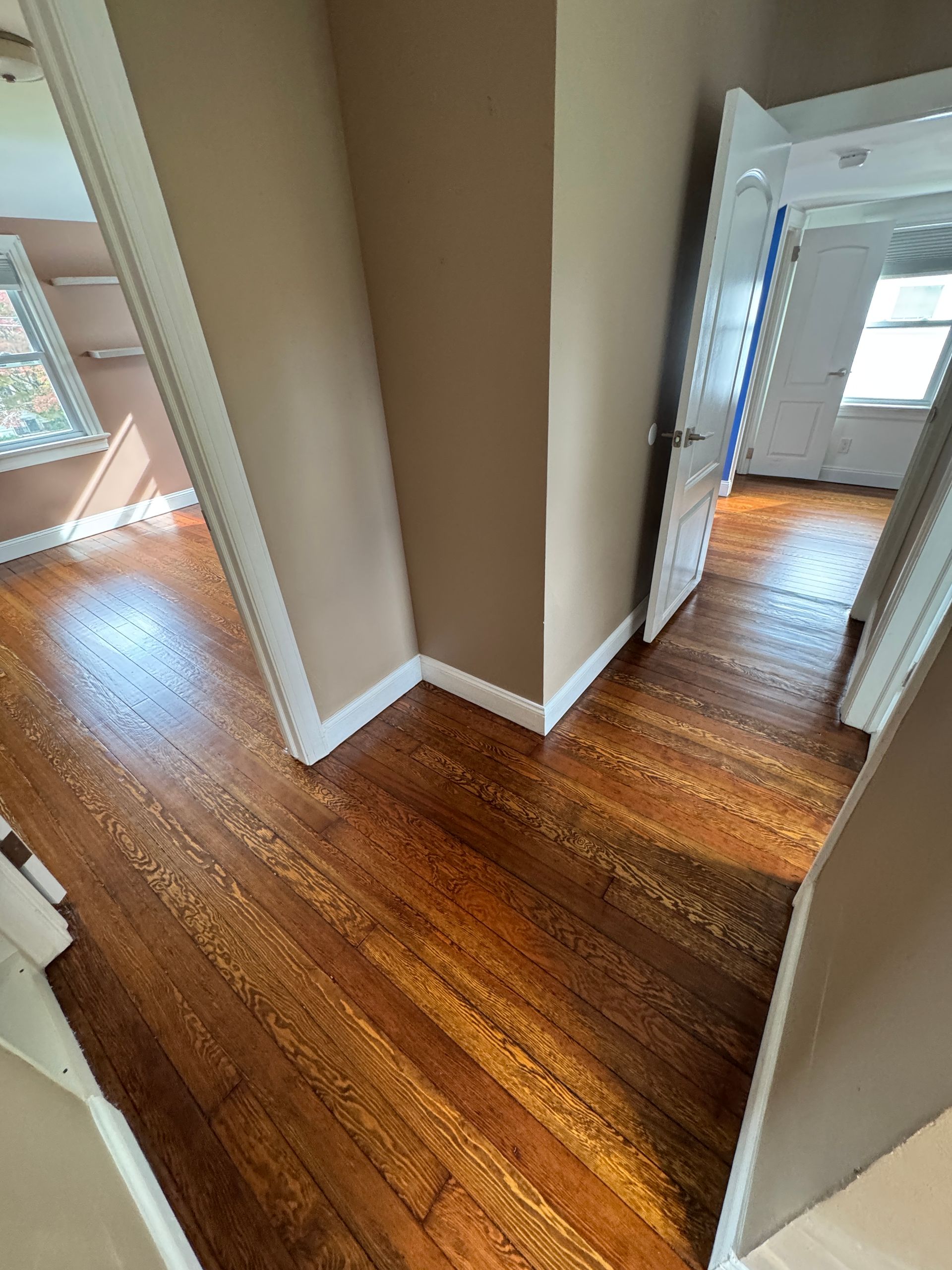 Empty hallway with glossy hardwood floors, beige walls, and white trim leading to rooms on both sides