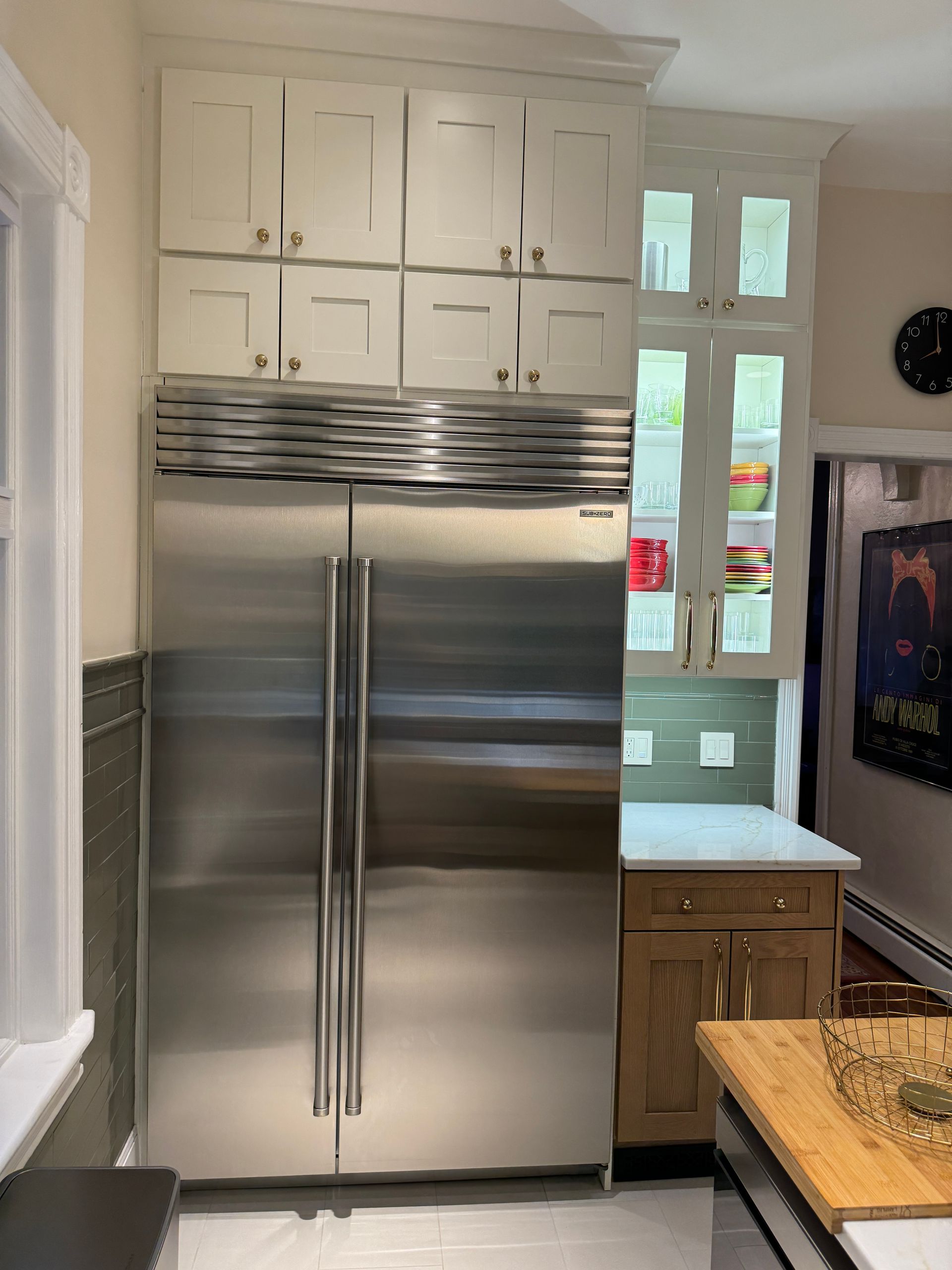Stainless steel refrigerator in a bright kitchen with white cabinets and a wood countertop island.