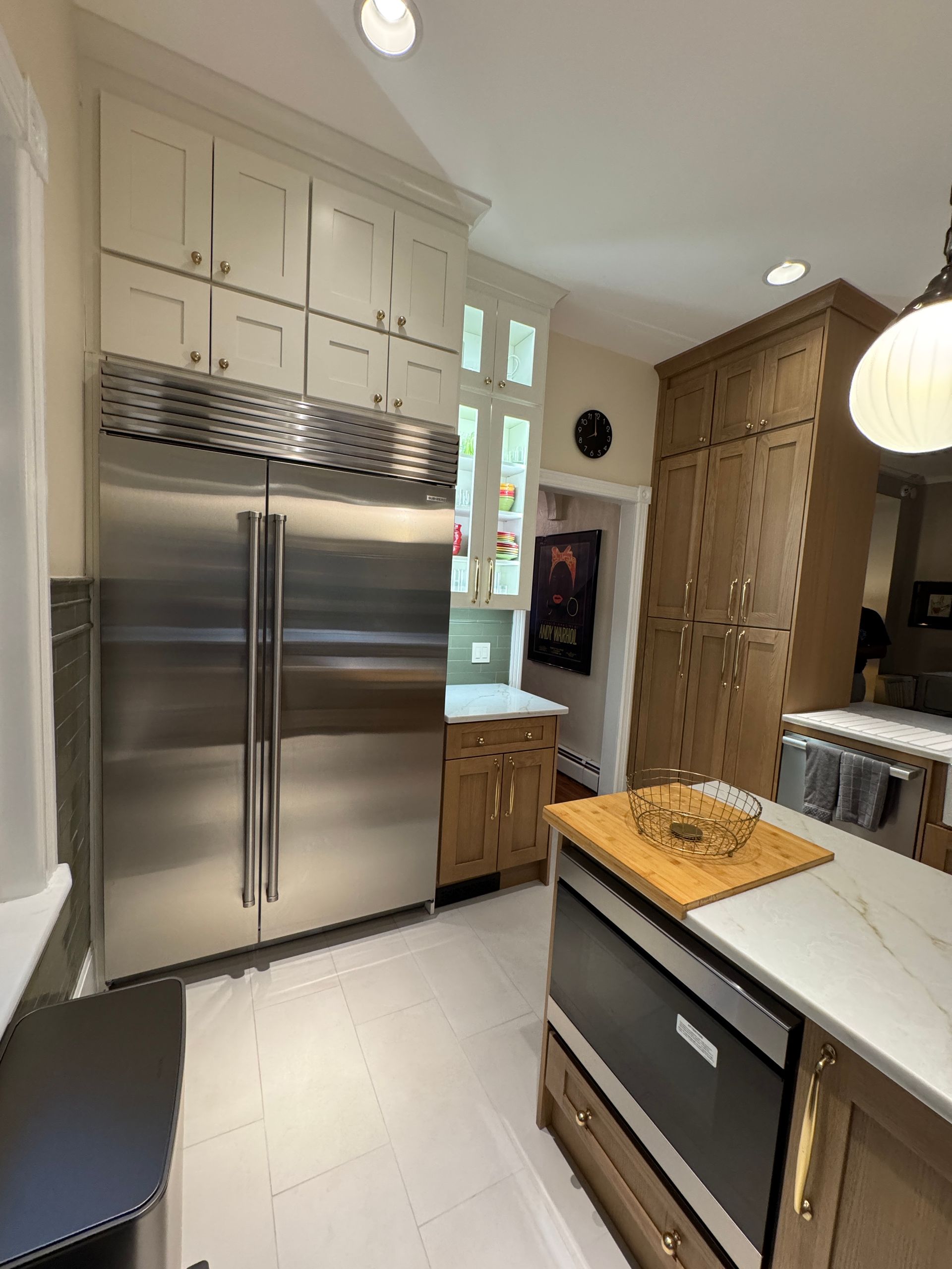 Bright modern kitchen with stainless steel fridge, white cabinets, island, and wood door panel wall.