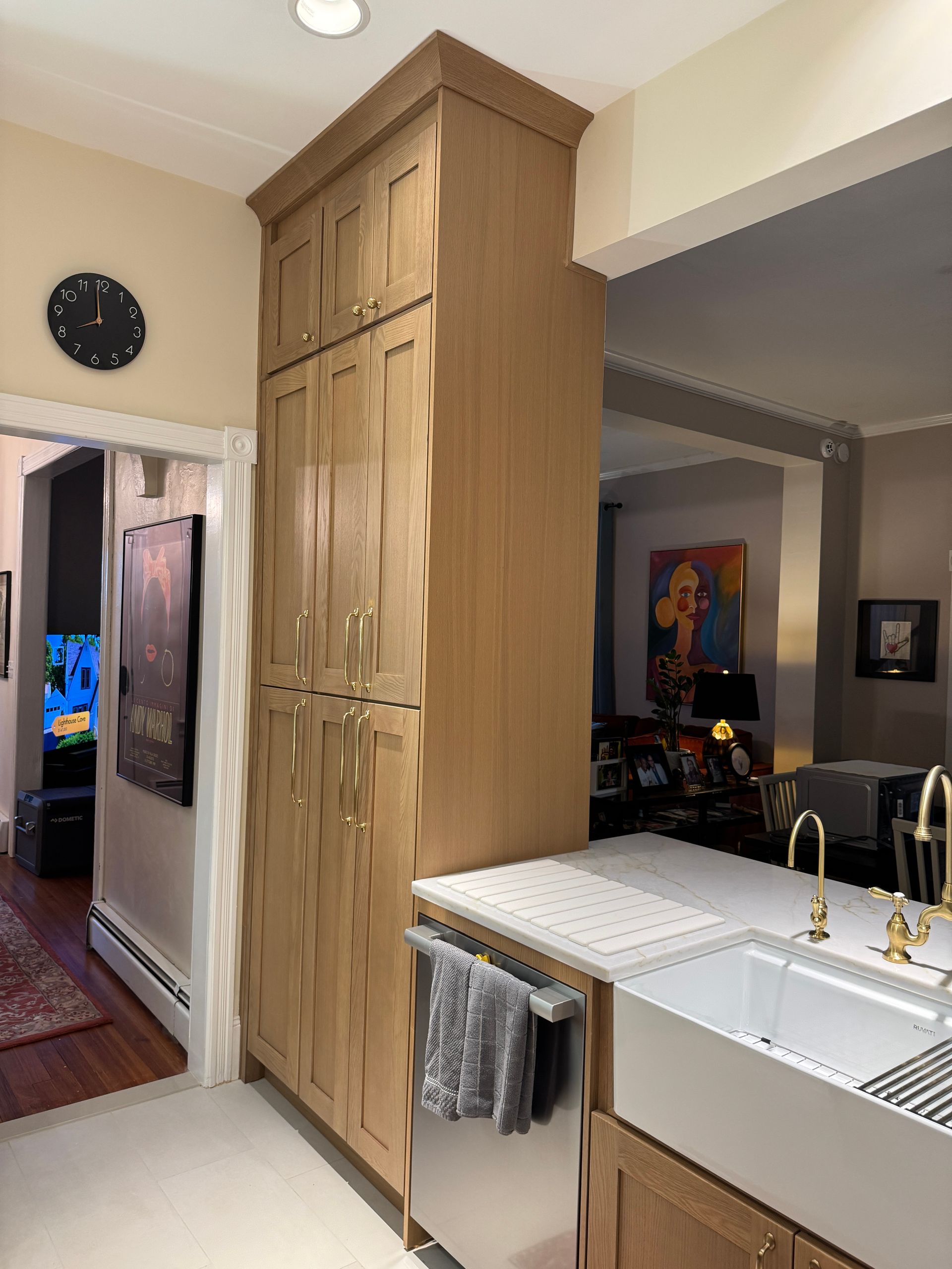 Modern kitchen with tall wood pantry cabinets, farmhouse sink, and a view into a living room.