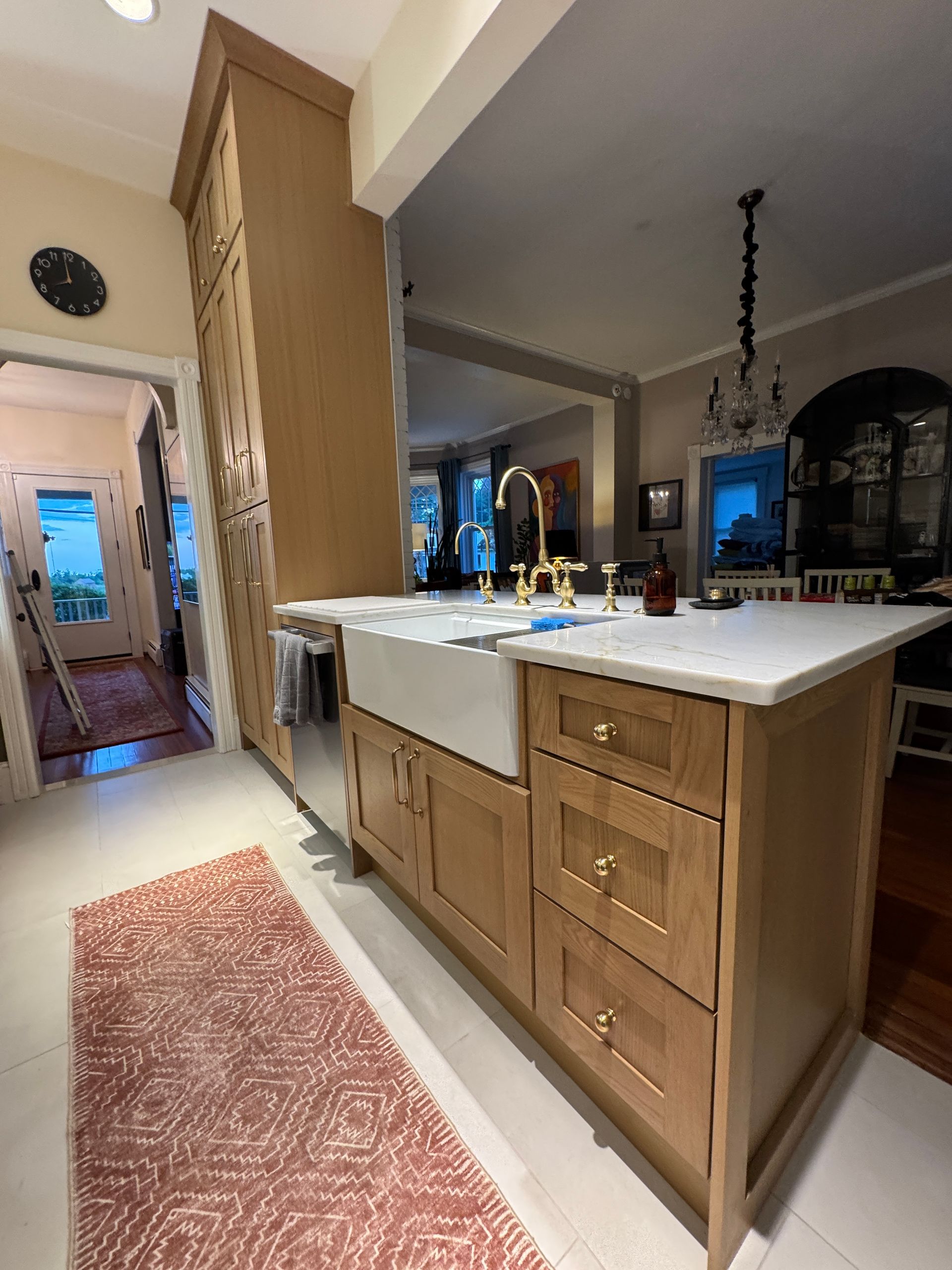 Kitchen with wood cabinets, white island countertop, and pink runner rug in a warmly lit open room