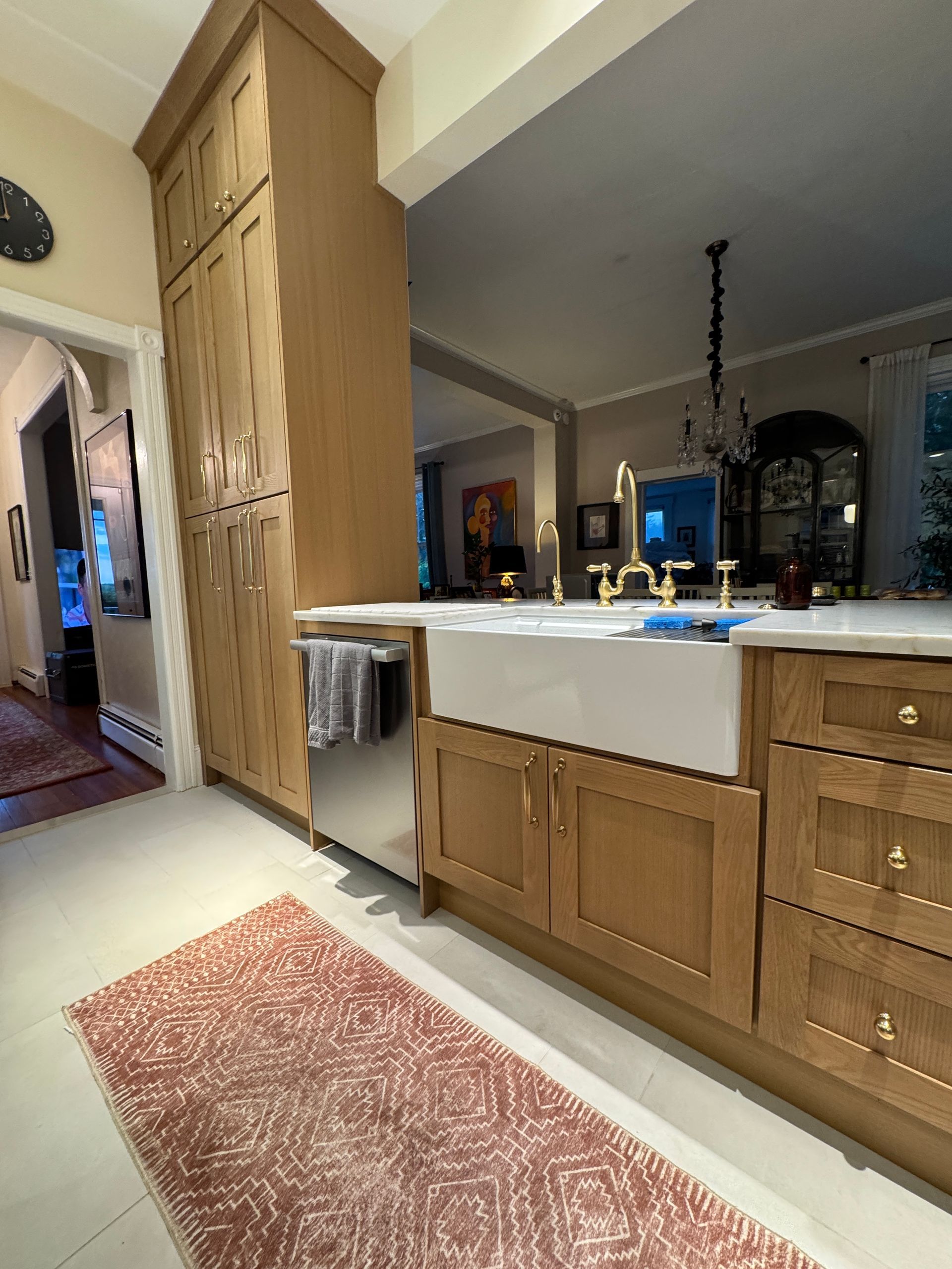 Kitchen with wooden cabinets, white island, and red rug, viewed from a hallway at night.